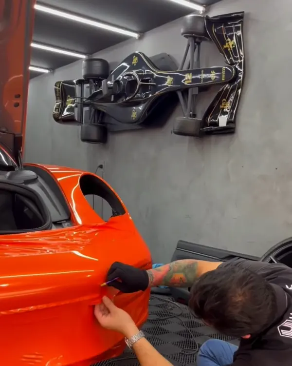 Técnico aplicando envelopamento laranja num Porsche 911 no piso técnico do estúdio
